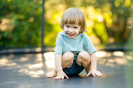 Cute toddler boy jumping on a trampoline in a backyard on warm and sunny summer day. Sports and exercises for children. Summer outdoor leisure activities.の写真素材