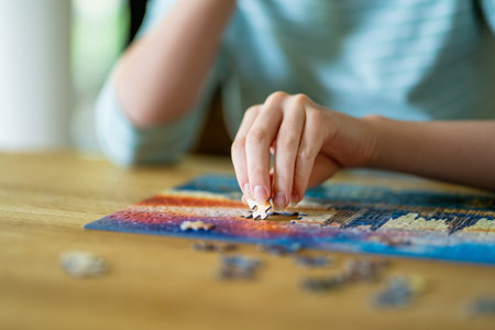 Close-up on woman hand playing puzzles at home. Connecting jigsaw puzzle pieces in a living room table, assembling a jigsaw puzzle. Fun family leisure.の写真素材