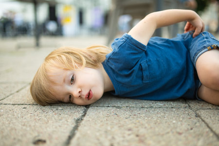 Toddler boy having a tamtrum laying on the ground outdoors. Misbehaving child on the street.の写真素材