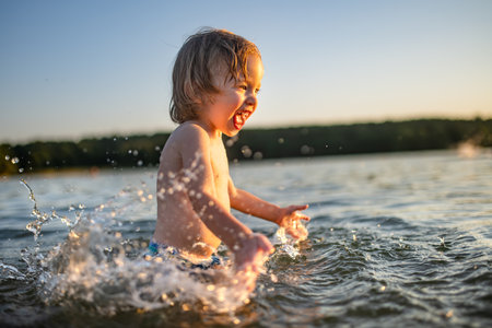 Cute toddler boy playing by a lake on hot summer day. Adorable child having fun outdoors during summer vacations. Water activities for kids.の写真素材