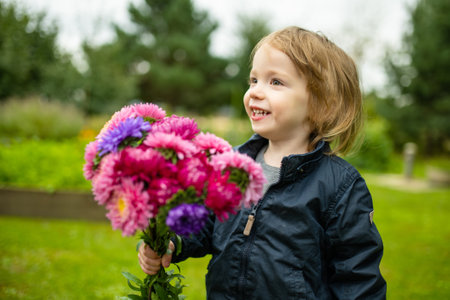Cute toddler boy holding a bunch of colourful aster flowers. Child picking fresh flowers in a garden...