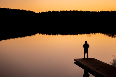 Silhouette of a hiker admiring beautiful waters of lake Gela on sunset. Birds eye view of scenic emerald lake surrounded by pine forests.の写真素材