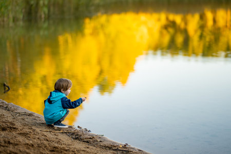 Adorable toddler boy having fun by the Gela lake on sunny fall day. Child exploring nature on autumn day in Vilnius, Lithuania. Fun autumn activities for kids.の写真素材