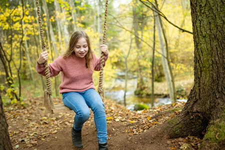 Pretty young girl having fun on a playground in beautiful autumn park. Cute preteen child playing outdoors in late autumn. Outdoor activities for family with kids.の写真素材