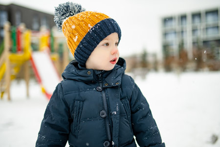 Adorable toddler boy having fun in a city on snowy winter day. Cute child wearing warm clothes playing in a snow. Winter activities for family with kids.の写真素材