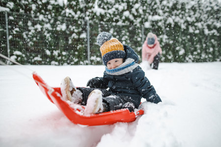 Funny toddler boy having fun with a sleigh in beautiful winter park. Cute child playing in a snow....