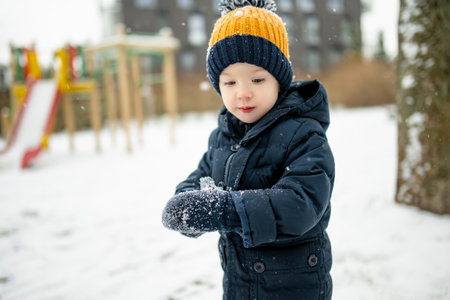 Adorable toddler boy having fun in a city on snowy winter day. Cute child wearing warm clothes playing in a snow. Winter activities for family with kids.の写真素材