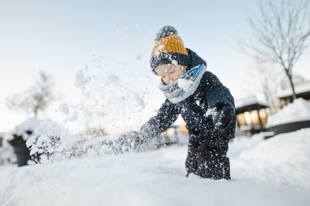 Adorable toddler boy having fun in a city on snowy winter day. Cute child wearing warm clothes playing in a snow. Winter activities for family with kids.の写真素材