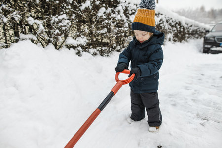 Adorable toddler boy helping his grandfather to shovel snow in a backyard on winter day. Cute child wearing warm clothes playing in a snow. Winter activities for family with kids.の写真素材