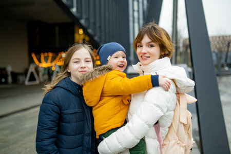 Two big sisters and their toddler brother having fun outdoors. Two young girls holding their sibling...