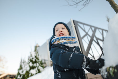 Adorable toddler boy having fun in a city on snowy winter day. Cute child wearing warm clothes playing in a snow. Winter activities for family with kids.の写真素材