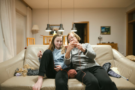 Grandmother and teenage granddaughter knitting on a sofa. Grandma teaching teen child to knit....