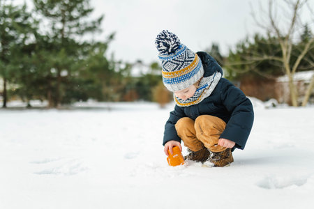 Adorable toddler boy having fun in a backyard on snowy winter day. Cute child wearing warm clothes playing in a snow. Winter activities for family with kids.の写真素材