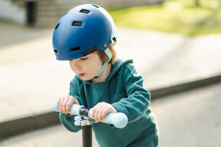 Adorable toddler boy riding his scooter in a city on sunny summer evening. Young child riding a roller. Active leisure and outdoor sports for kids.の写真素材