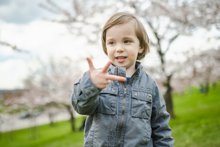 Cute toddler boy playing in blooming cherry tree garden on beautiful spring day. Adorable baby...