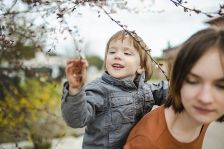 Pretty teenage girl and her toddler brother having fun in blooming cherry tree garden on beautiful spring day. Kids exploring nature. Big age difference between siblings.の写真素材