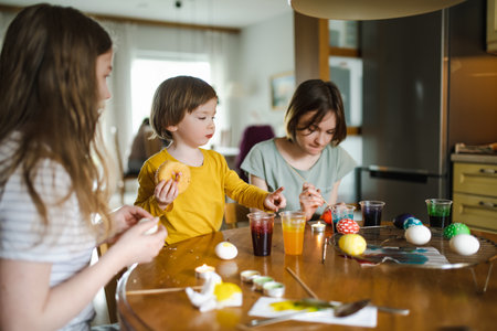 Two big sisters and their little brother dyeing Easter eggs at home. Children painting colorful eggs for Easter hunt. Kids getting ready for Easter celebration. Family traditions.の写真素材