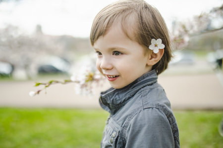 Cute toddler boy playing in blooming cherry tree garden on beautiful spring day. Adorable baby...