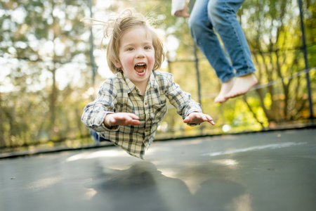 Cute little boy jumping on a trampoline in a backyard on warm and sunny summer day. Sports and exercises for children. Summer outdoor leisure activities.の写真素材