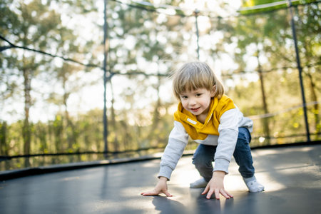 Cute little boy jumping on a trampoline in a backyard on warm and sunny summer day. Sports and exercises for children. Summer outdoor leisure activities.の写真素材