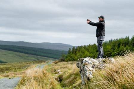 Tourist taking a photo at Glengesh Pass, stunning mountain pass road in west Donegal between the...