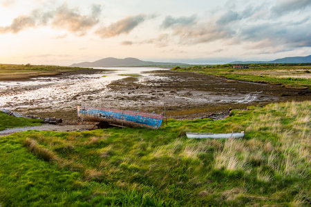 Old boat left on a small beach along the Ring of Kerry route. Rugged coast of on Iveragh Peninsula on sunset, County Kerry, Ireland.の写真素材