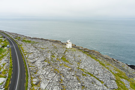 Black Head Lighthouse, situated in the rough rocky landscape of Burren, amidst a bizarre scenery of steep limestone mountains and rocky coastline, County Clare, Ireland.の写真素材