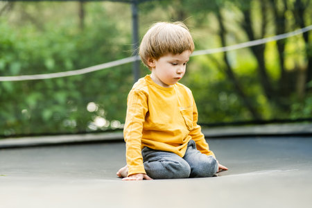 Cute little boy jumping on a trampoline in a backyard on warm and sunny summer day. Sports and exercises for children. Summer outdoor leisure activities.の写真素材