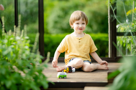 Cute toddler boy having fun in a greenhouse on sunny summer day. Child helping with daily chores. Gardening activity for kids.の写真素材