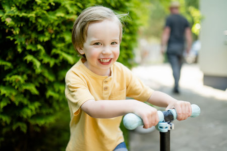 Adorable little boy riding his scooter in a back yard on sunny summer evening. Young child riding a roller. Active leisure and outdoor sports for kids.の写真素材