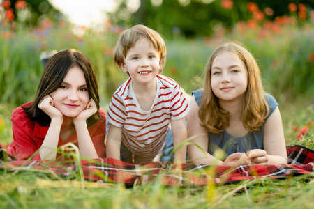 Beautiful teenage girls and their toddler brother admiring poppy and knapweed flowers in blossoming poppy field on sunny summer day.の写真素材
