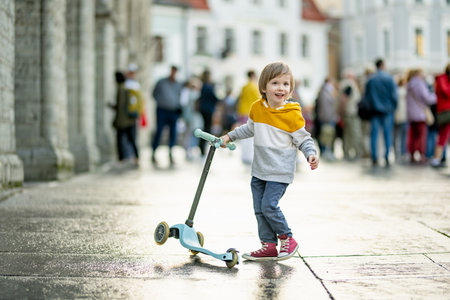 Cute little boy riding his baby scooter along colorful medieval streets of Tallinn Old Town or Tallinna Valalinn, included in the UNESCO World Heritage List. Child exploring Estonian capital.の写真素材