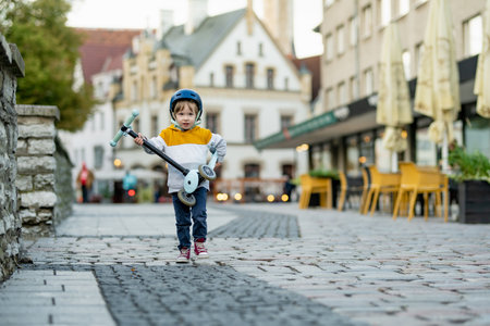Cute little boy riding his baby scooter along colorful medieval streets of Tallinn Old Town or Tallinna Valalinn, included in the UNESCO World Heritage List. Child exploring Estonian capital.の写真素材