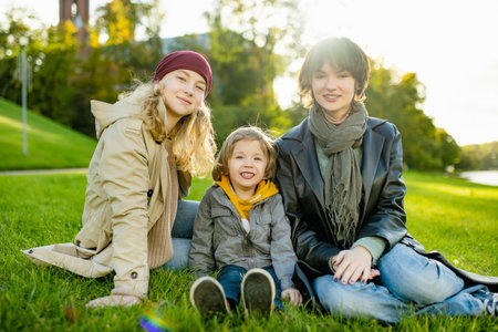 Two big sisters and their toddler brother having fun outdoors. Two young girls with a toddler boy on...