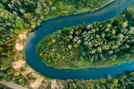 Aerial view of Sventoji river winding through autumn forest. Beautiful aerial forest scene near Anyksciai, Lithuania. Green trees and river on sunny fall day.の写真素材