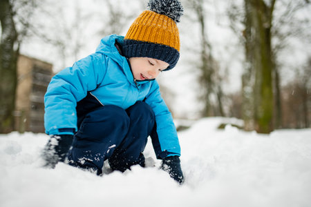 Adorable toddler boy having fun in a city on snowy winter day. Cute child wearing warm clothes playing in a snow. Winter activities for family with kids.の写真素材