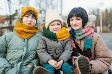 Two big sisters and their toddler brother having fun outdoors. Two young girls holding their sibling boy on winter day. Kids during winter break. Children exploring nature together.の写真素材