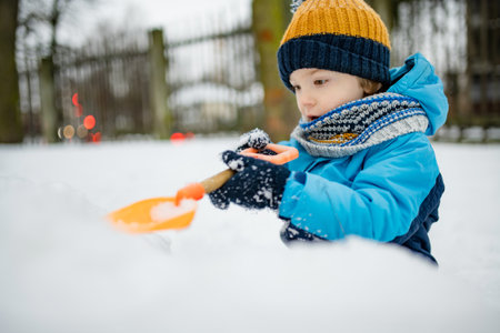 Adorable little boy having fun on snowy winter day. Cute child wearing warm clothes playing in a snow. Winter activities for family with kids.の写真素材