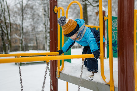 Adorable little boy having fun on a playground on snowy winter day. Cute child wearing warm clothes playing in a snow. Winter activities for family with kids.の写真素材