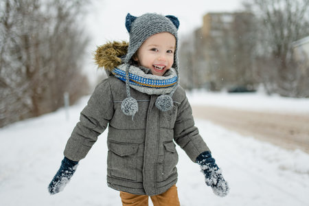 Adorable little boy having fun on snowy winter day. Cute child wearing warm clothes playing in a snow. Winter activities for family with kids.の写真素材