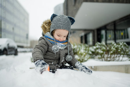 Adorable little boy having fun in a city on snowy winter day. Cute child wearing warm clothes playing in a snow. Winter activities for family with kids.の写真素材
