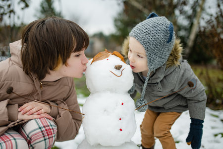 Adorable teenage girl and her little brother building a snowman in the backyard. Cute children playing in a snow. Fun winter activities for family with kids.の写真素材