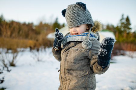 Adorable little boy having fun on snowy winter day. Cute child wearing warm clothes playing in a snow. Winter activities for family with kids.の写真素材