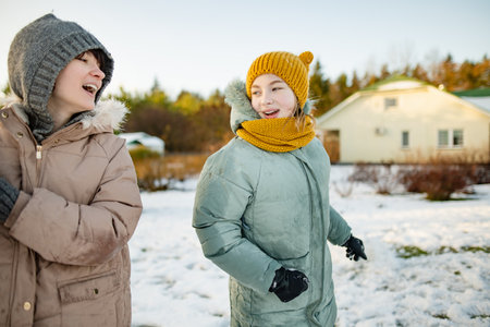 Adorable teenage girls building a snowman in the backyard. Cute children playing in a snow. Fun...