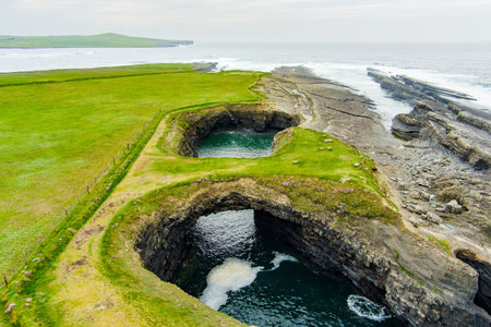 Aerial view of Bridges of Ross, three natural rock arches, carved into the cliffs by natural ocean erosion, on the west coast of Ross Bay, Wild Atlantic Way Discovery Point, County Clare, Irelandの写真素材