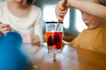 Big sister and her little brother dyeing Easter eggs at home. Children painting colorful eggs for Easter hunt. Kids getting ready for Easter celebration. Family traditions.の写真素材