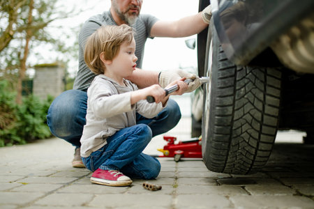 Cute little boy helping his father to change car wheels at their backyard. Father teaching his little son to use tools. Active parent of a small child.の写真素材