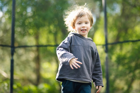 Cute little boy jumping on a trampoline in a backyard on warm and sunny summer day. Sports and exercises for children. Summer outdoor leisure activities.の写真素材