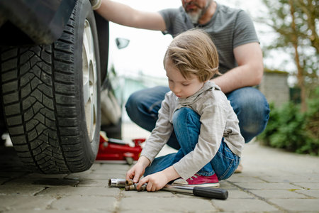 Cute little boy helping his father to change car wheels at their backyard. Father teaching his little son to use tools. Active parent of a small child.の写真素材