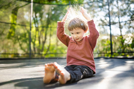 Cute little boy jumping on a trampoline in a backyard on warm and sunny summer day. Sports and exercises for children. Summer outdoor leisure activities.の写真素材